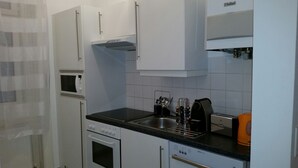 A compact kitchen with white cabinets, a built-in oven, a microwave, a sink, and a toaster. - Goldfisch Apartment Central Park (Vienna)