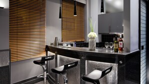Cocina moderna con barra, destacando una encimera negra, dos taburetes de bar, un florero con flores y una botella de vino.