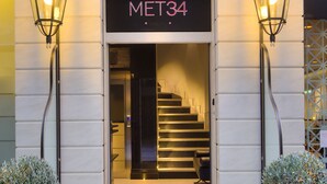 Entrada de hotel con una escalera que conduce al interior, un letrero que dice "MET34" y dos macetas a cada lado.