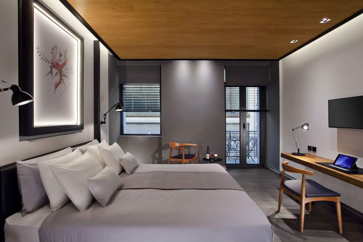 Quarto de hotel moderno com cama, escrivaninha, cadeira e televisão.