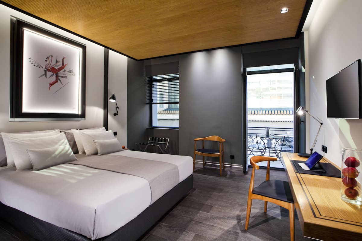Quarto de hotel moderno com uma cama grande, uma escrivaninha com um laptop, uma cadeira e uma televisão.