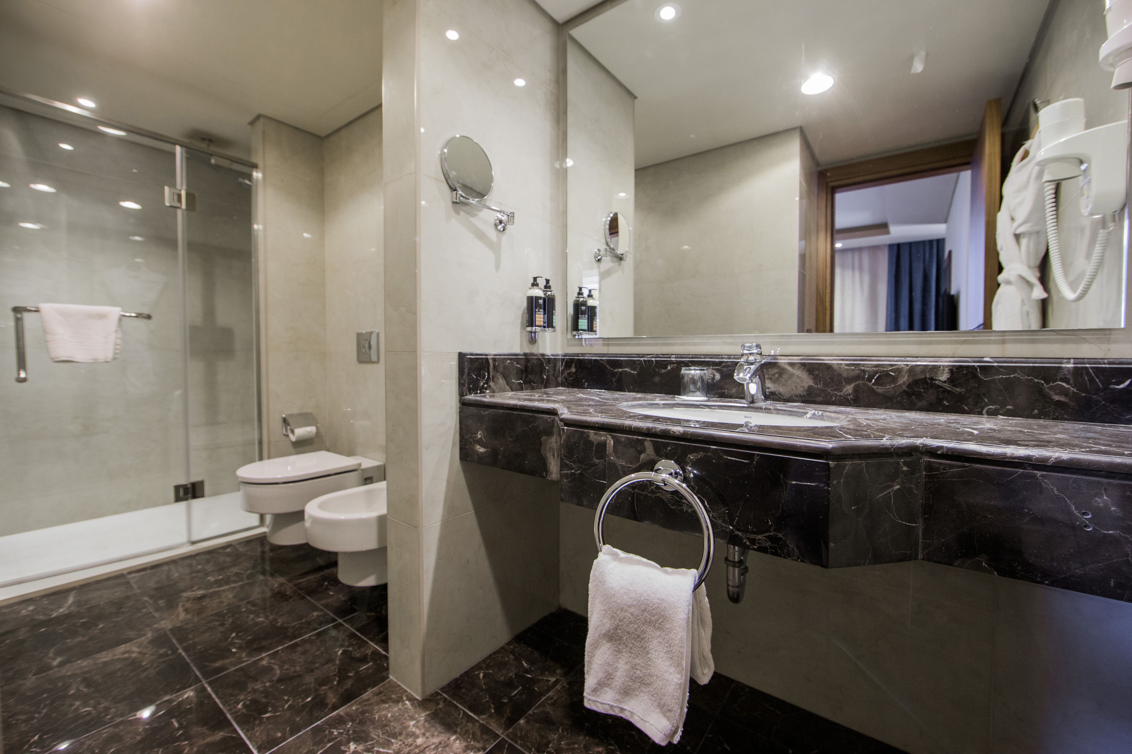A modern bathroom with a glass-enclosed shower, a marble sink, and a large mirror.