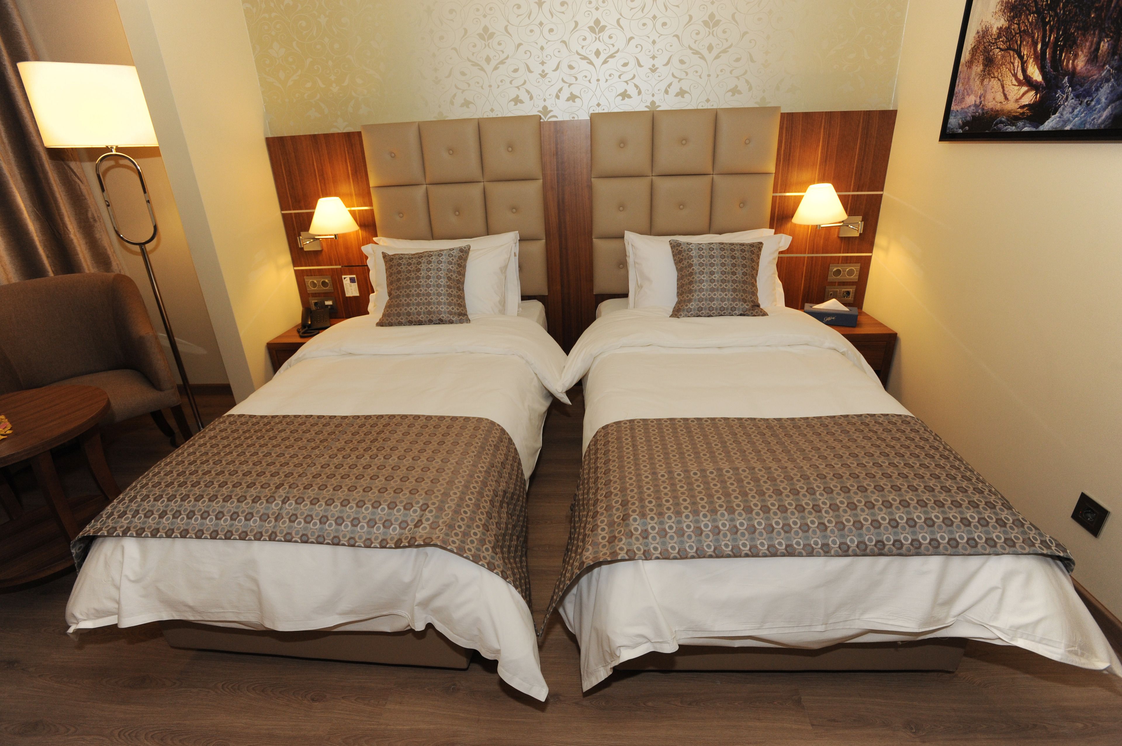 A double bed with a wooden headboard, two bedside tables with lamps, a chair, and a patterned bedspread.