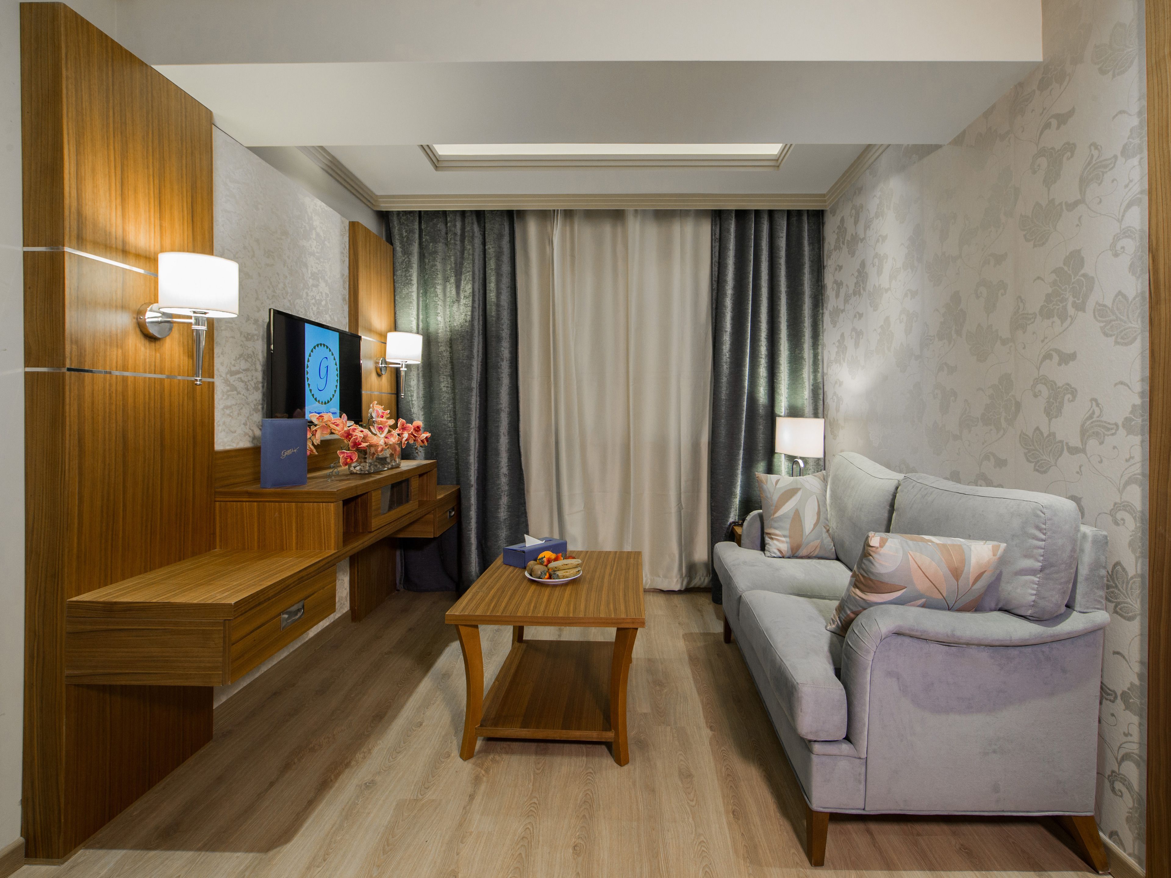 A modern hotel room with a wooden desk, a sofa, a small table, and a TV.