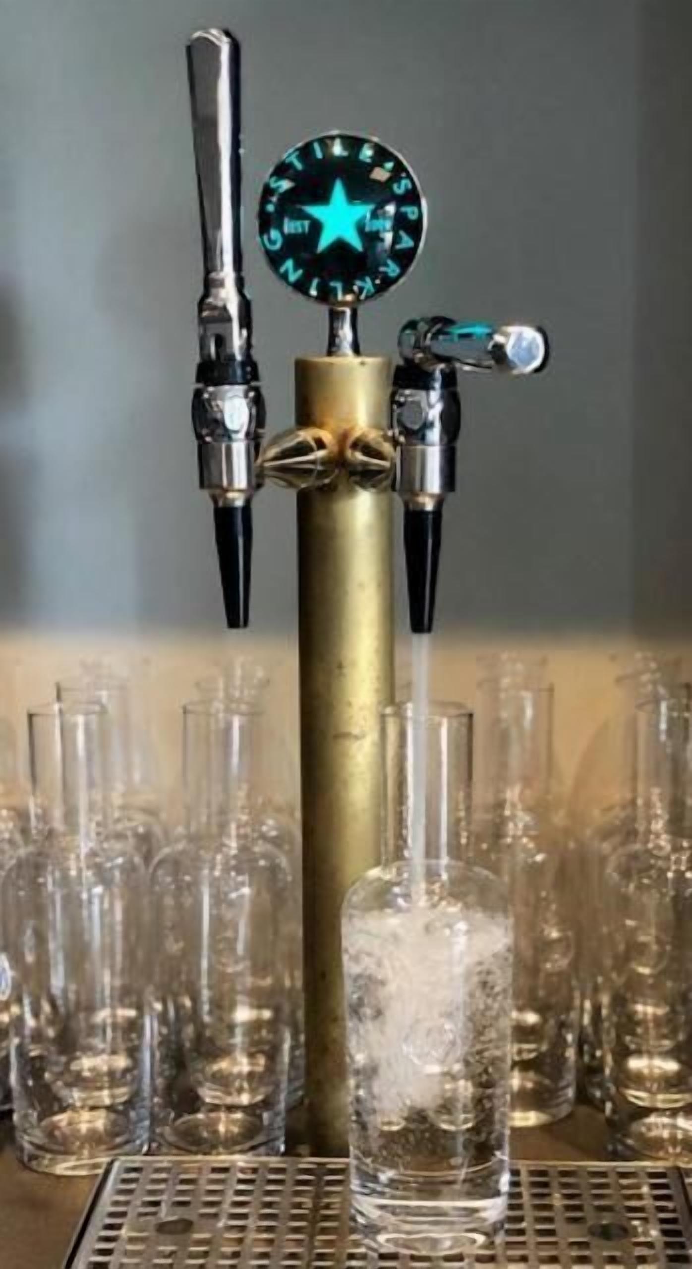 A tap with a star-shaped spigot and a pressure gauge, surrounded by empty glasses on a tray.