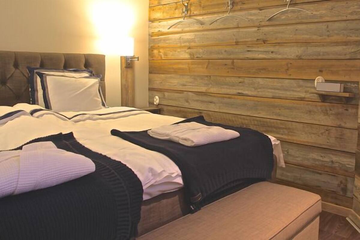 A hotel room with a wooden wall panel design, a tufted headboard, and a bedside table with a lamp.