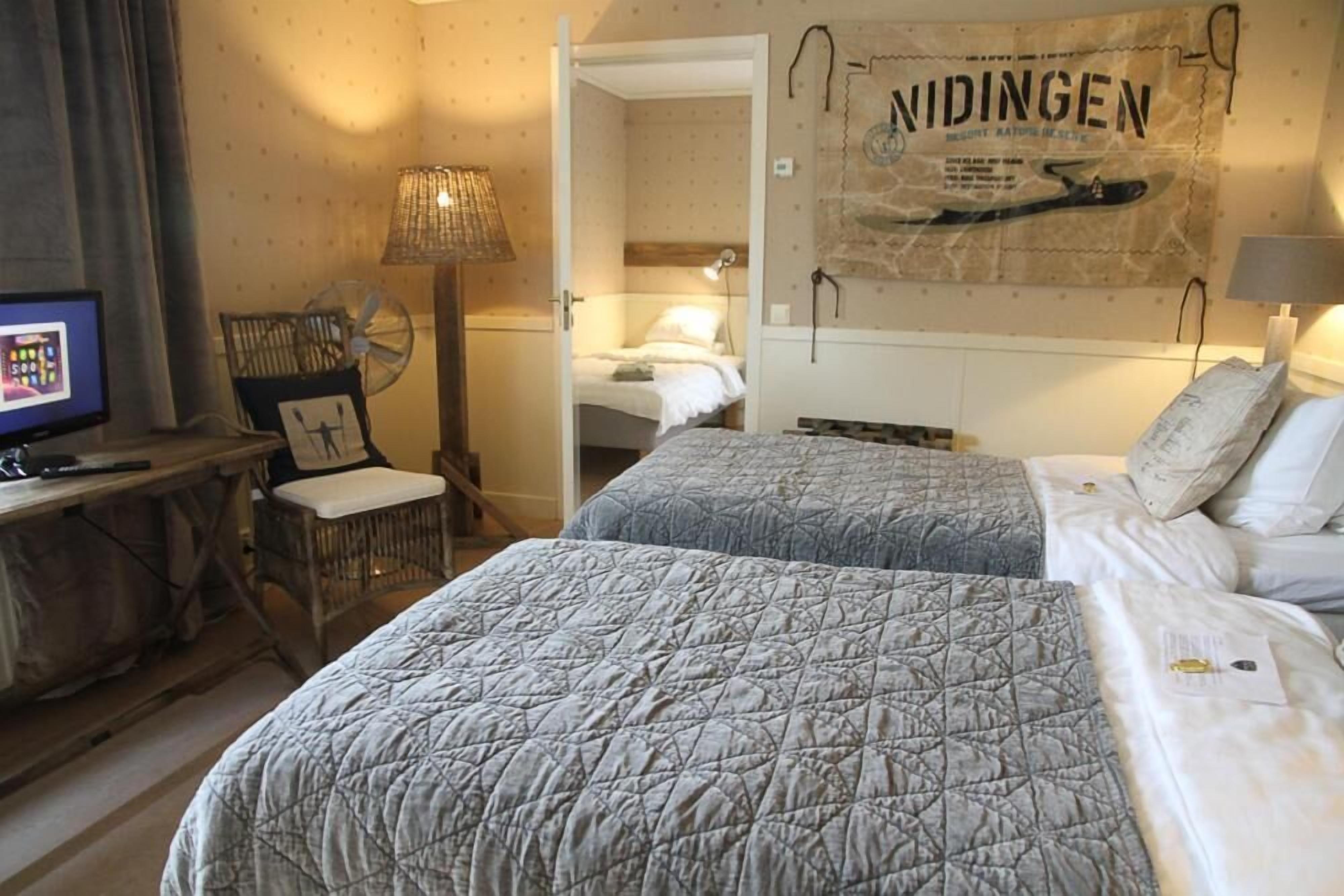 Une chambre d’hôtel avec deux lits, un bureau avec un ordinateur, une chaise et un mur orné d’une affiche.