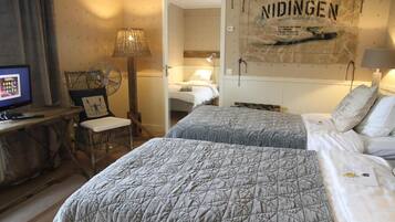 Une chambre d’hôtel avec deux lits, un bureau avec un ordinateur, une chaise et un mur orné d’une affiche.