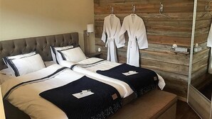 A double bed with a tufted headboard, two bedside tables, and a wooden wall with a mirror and two white robes hanging on a rack. - Gottskär Hotell & Konferens  (Gottskar)