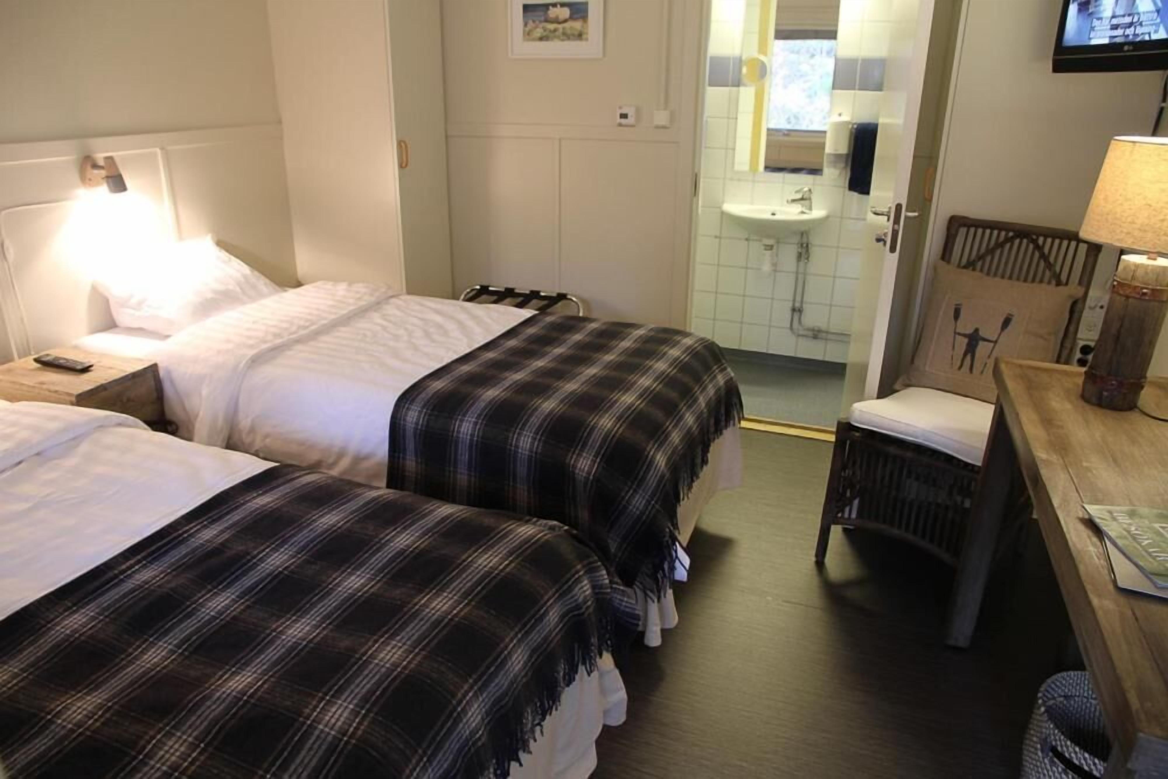 Een hotelkamer met twee bedden, een houten nachtkastje met een lamp, een stoel, een houten bureau met een lamp en een televisie aan de muur.