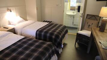 Een hotelkamer met twee bedden, een houten nachtkastje met een lamp, een stoel, een houten bureau met een lamp en een televisie aan de muur.