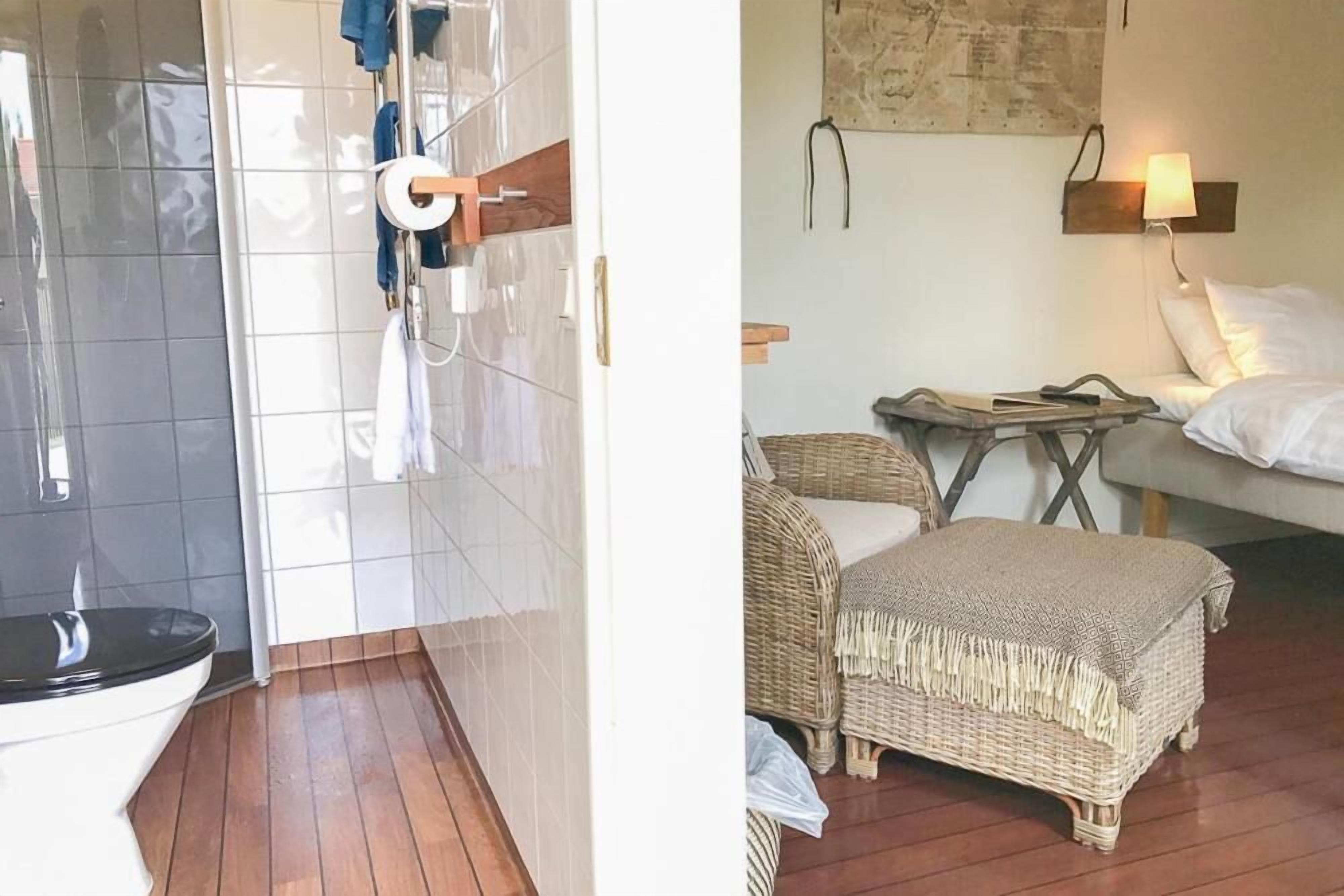 A bathroom with a toilet, a shower area, and a small table with a lamp.