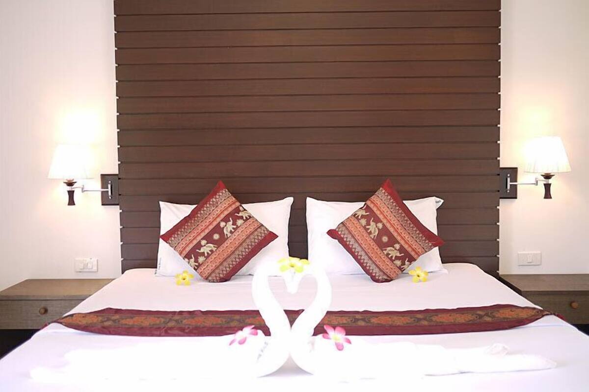 A hotel room with a large bed, two pillows with decorative patterns, bedside lamps, and a decorative swan arrangement on the bed.