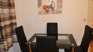 Een eethoek met een tafel met glazen blad en vier zwarte stoelen. Op de muur hangt een schilderij van een vaas met bloemen.