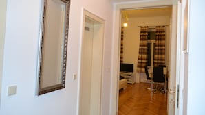 Een hal met een grote spiegel, een deur naar een kamer met een televisie, een eethoek met een tafel en stoelen, en een raam met gordijnen.