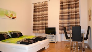 Een slaapkamer met een bed, een televisie op een standaard, een bureau met een stoel en gordijnen.