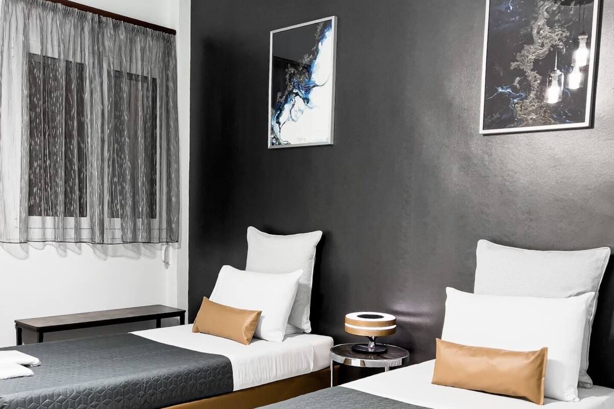 Ein modernes Hotelzimmer mit zwei Einzelbetten, einem kleinen Nachttisch und einem großen Fenster mit Vorhängen.