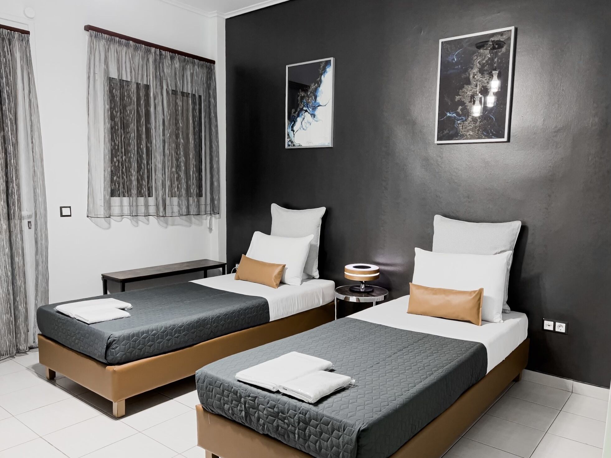 Habitación de hotel moderna con dos camas individuales, una mesita de noche con lámpara y obras de arte en las paredes.