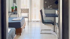 A modern hotel room with two beds, a kitchenette, and a large window with curtains.