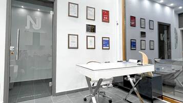 Un interior de oficina moderno con un escritorio de vidrio, certificados enmarcados en la pared y un espejo grande que refleja la habitación.