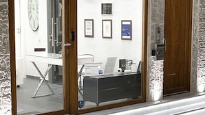 A reception area with a glass door, framed certificates on the wall, a clock, and a reception desk.