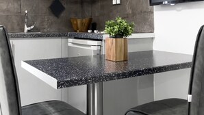 A modern kitchen with white cabinets, a black countertop, and two black chairs.