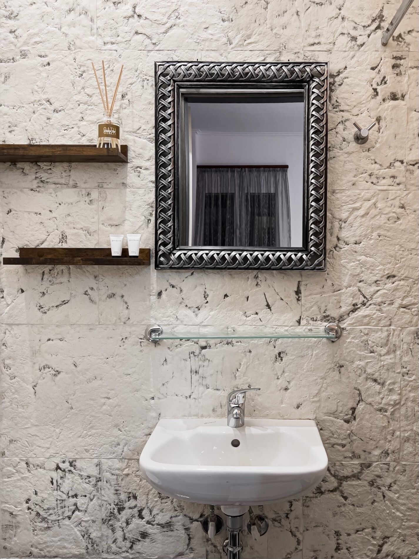 Un baño con un lavamanos blanco, un espejo con marco decorativo y un estante con artículos de aseo.