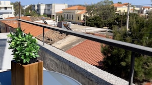 A balcony with a potted plant, a glass table, and a view of buildings and trees.