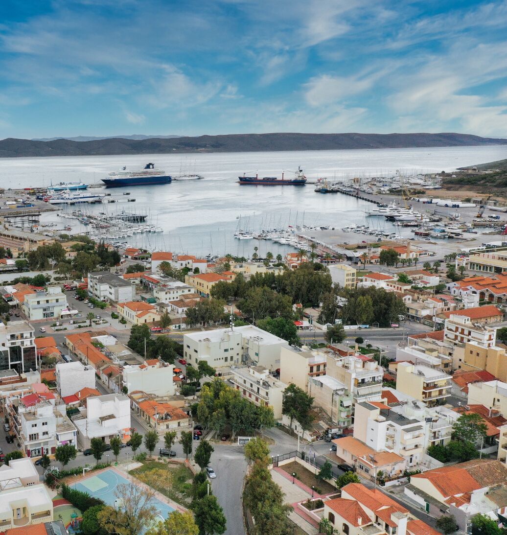 A coastal town with a marina filled with boats, surrounded by residential buildings with red-tiled roofs.