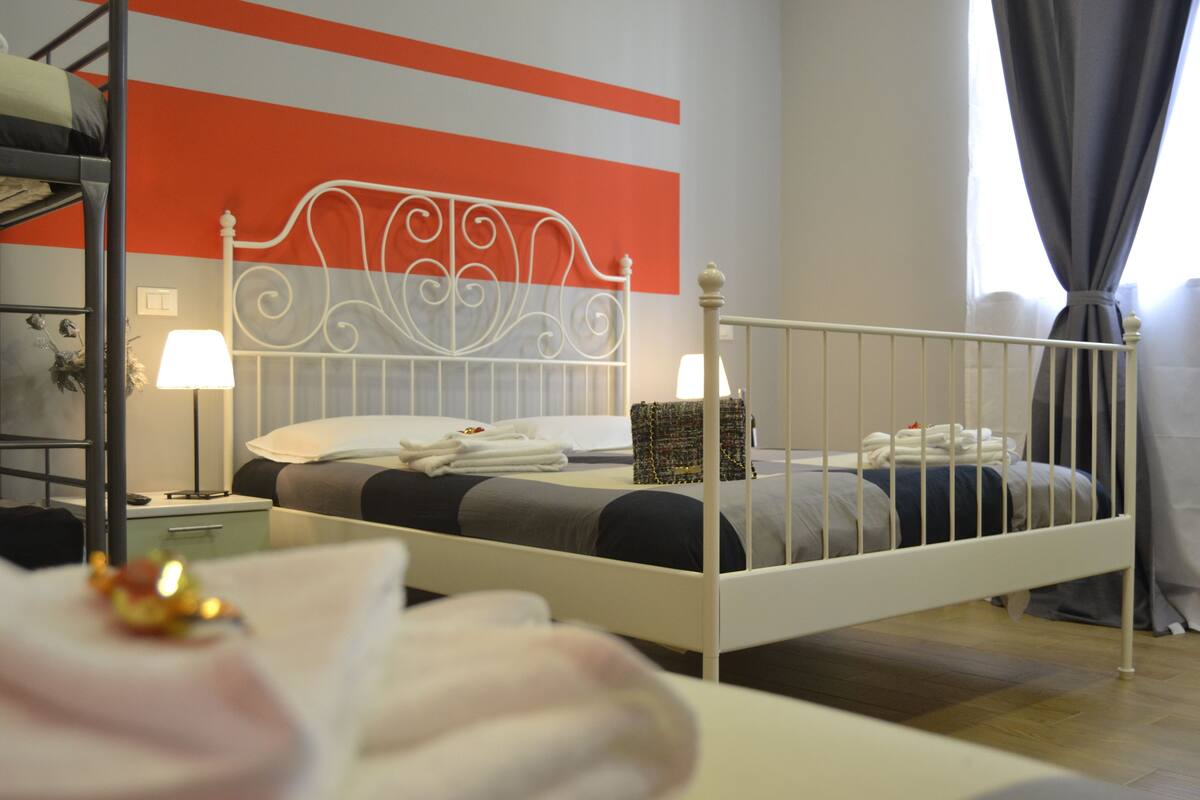 A single bed with a white metal headboard, a bedside table with a lamp, and a wall with a striped pattern.