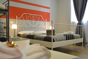 A single bed with a white metal headboard, a bedside table with a lamp, and a wall with a striped pattern.