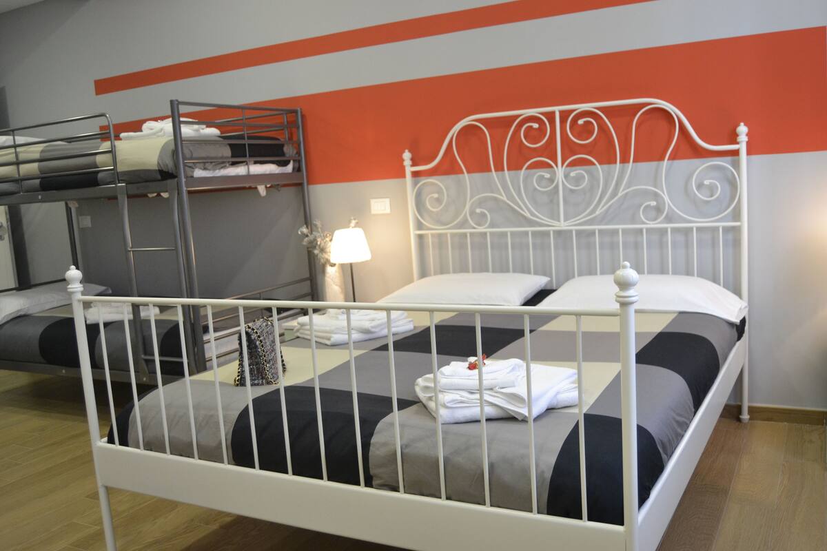 A single bed with a metal frame, a bunk bed above, and a wall with orange and grey stripes.