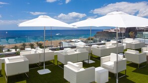 A rooftop lounge with white wicker furniture and umbrellas, overlooking a beach and ocean. - R2 Bahía Kontiki Beach Apartments (Tías)