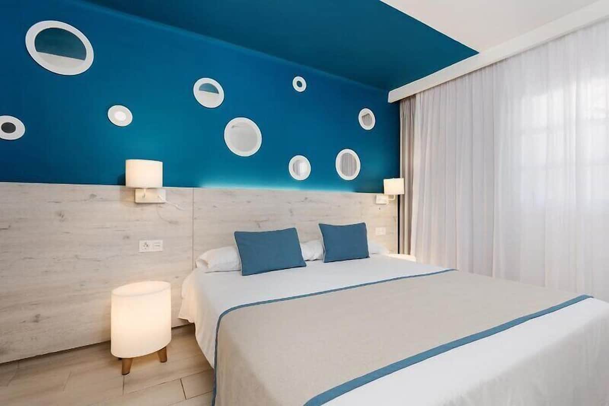 A hotel room with a bed, a nightstand, a lamp, and a wall with circular cutouts.