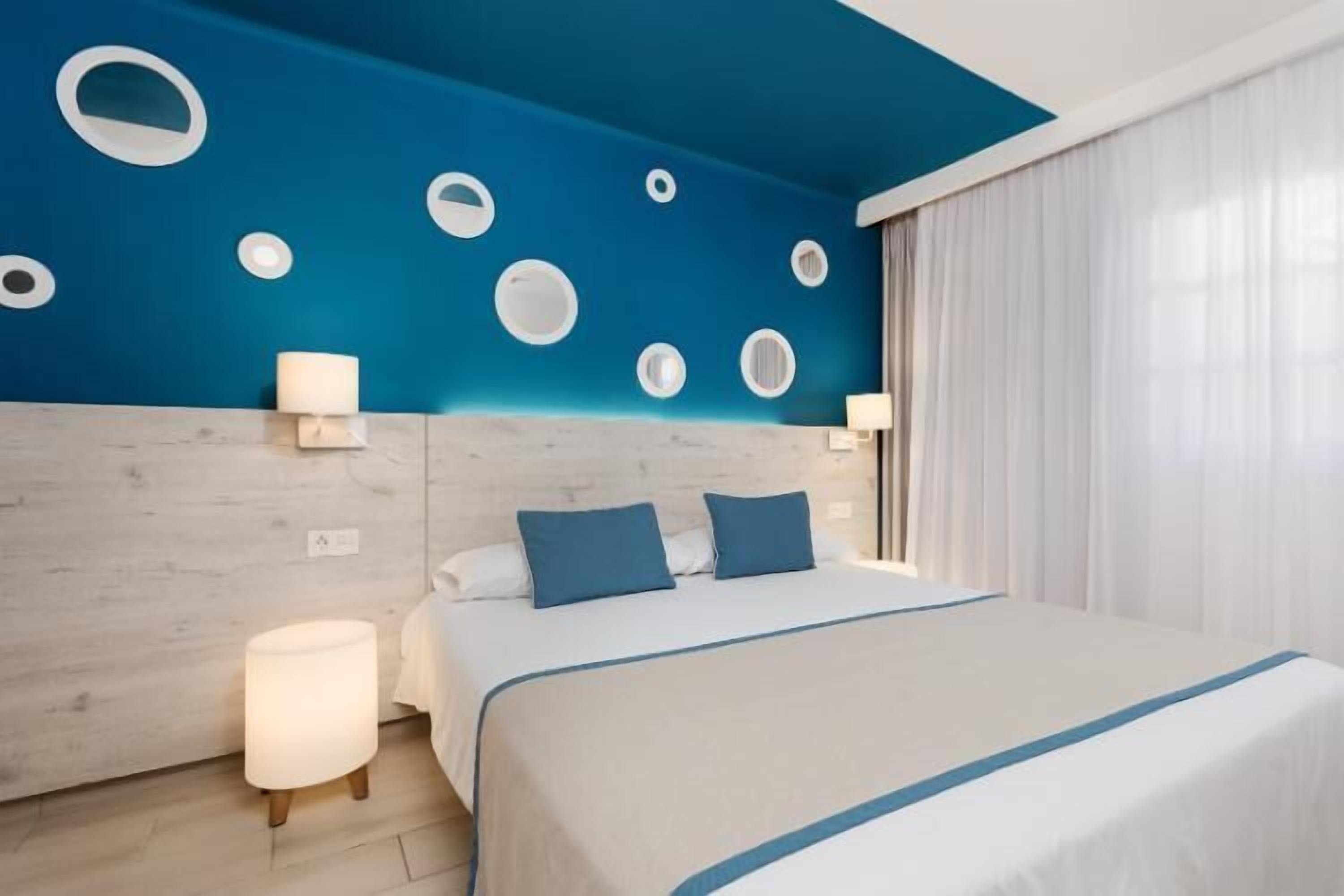 Una habitación de hotel con una cama, una mesita de noche, una lámpara y una pared con abertura circulares.