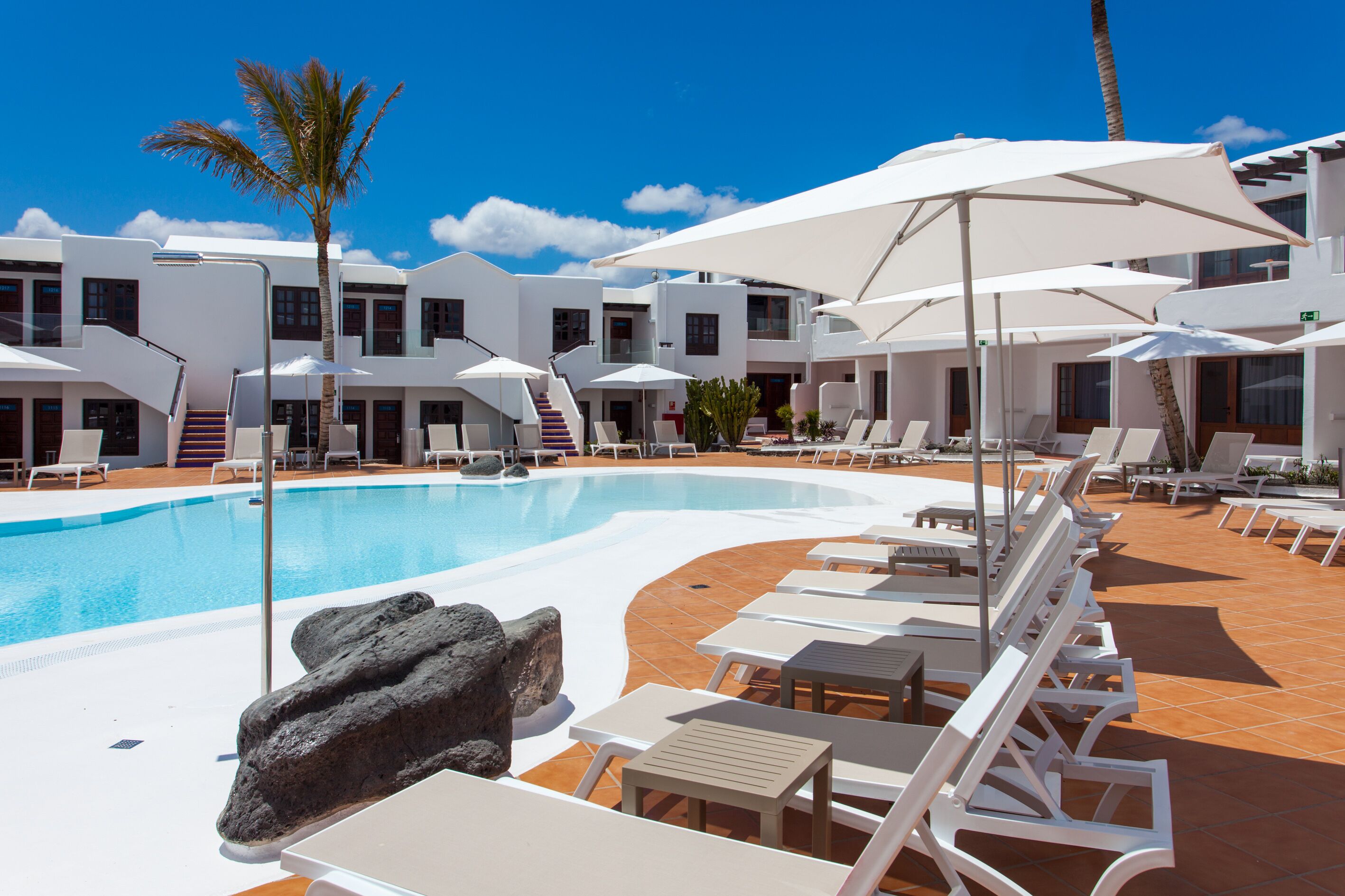 A poolside area with lounge chairs, umbrellas, and a clear blue sky.