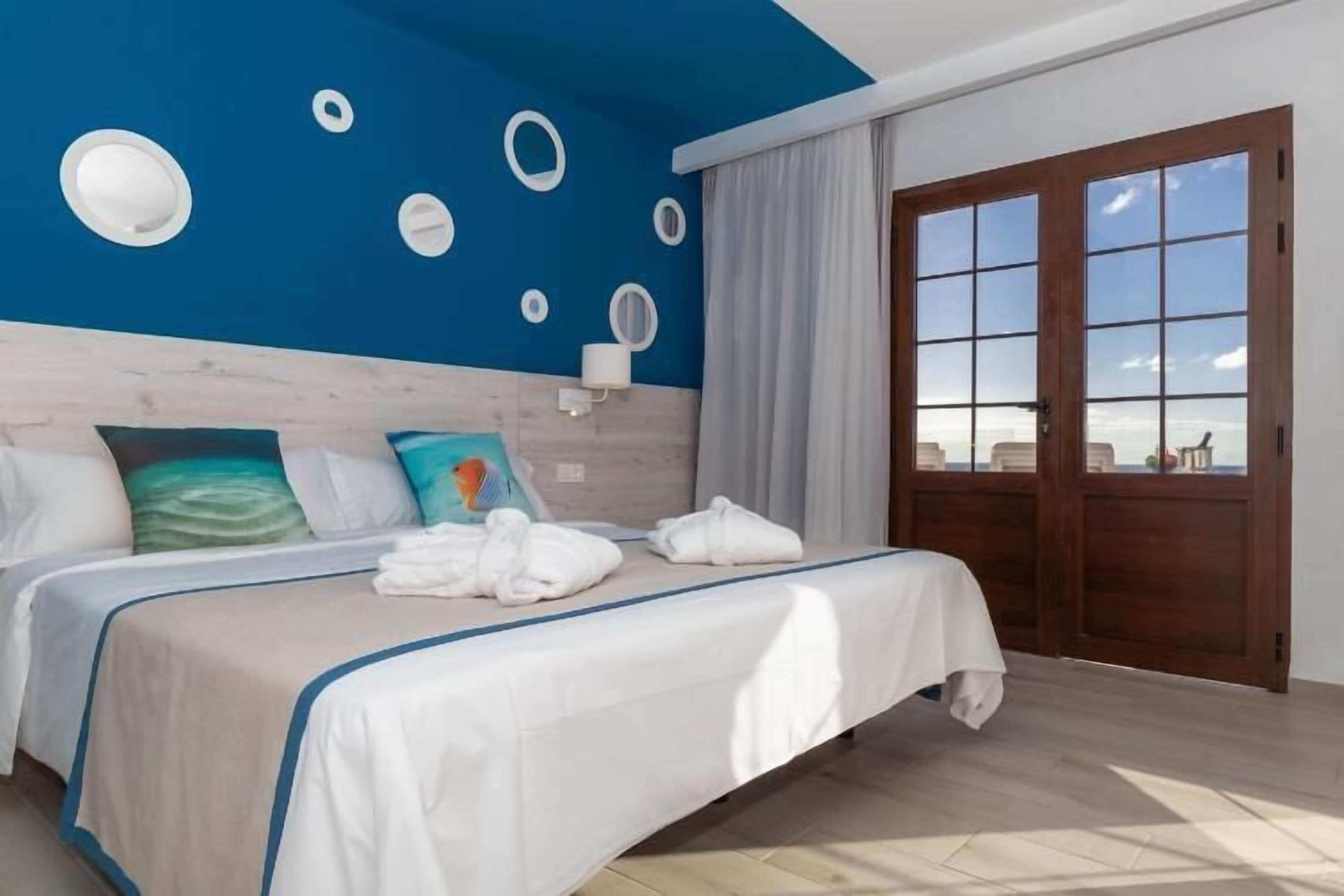 A bedroom with a bed, pillows, a nightstand, a window, and a view of the outside.