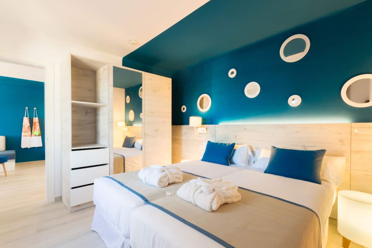 A modern hotel room with a large bed, a walk-in closet, and a blue accent wall with circular light fixtures.