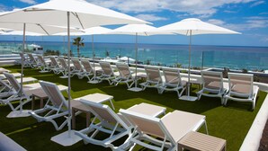 A rooftop lounge area with white lounge chairs and tables, white umbrellas, and a view of the ocean. - R2 Bahía Kontiki Beach Apartments (Tías)