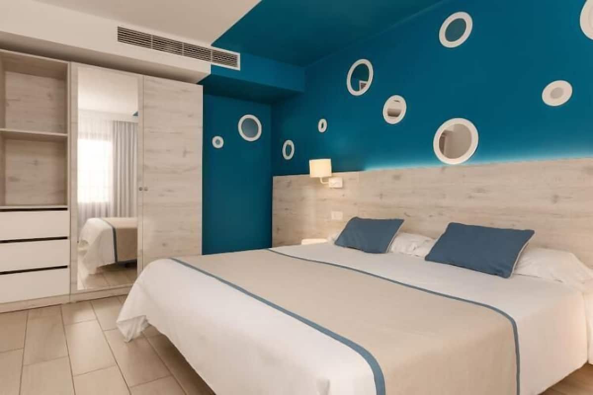 A hotel room with a bed, a wardrobe, and a wall with circular cutouts.