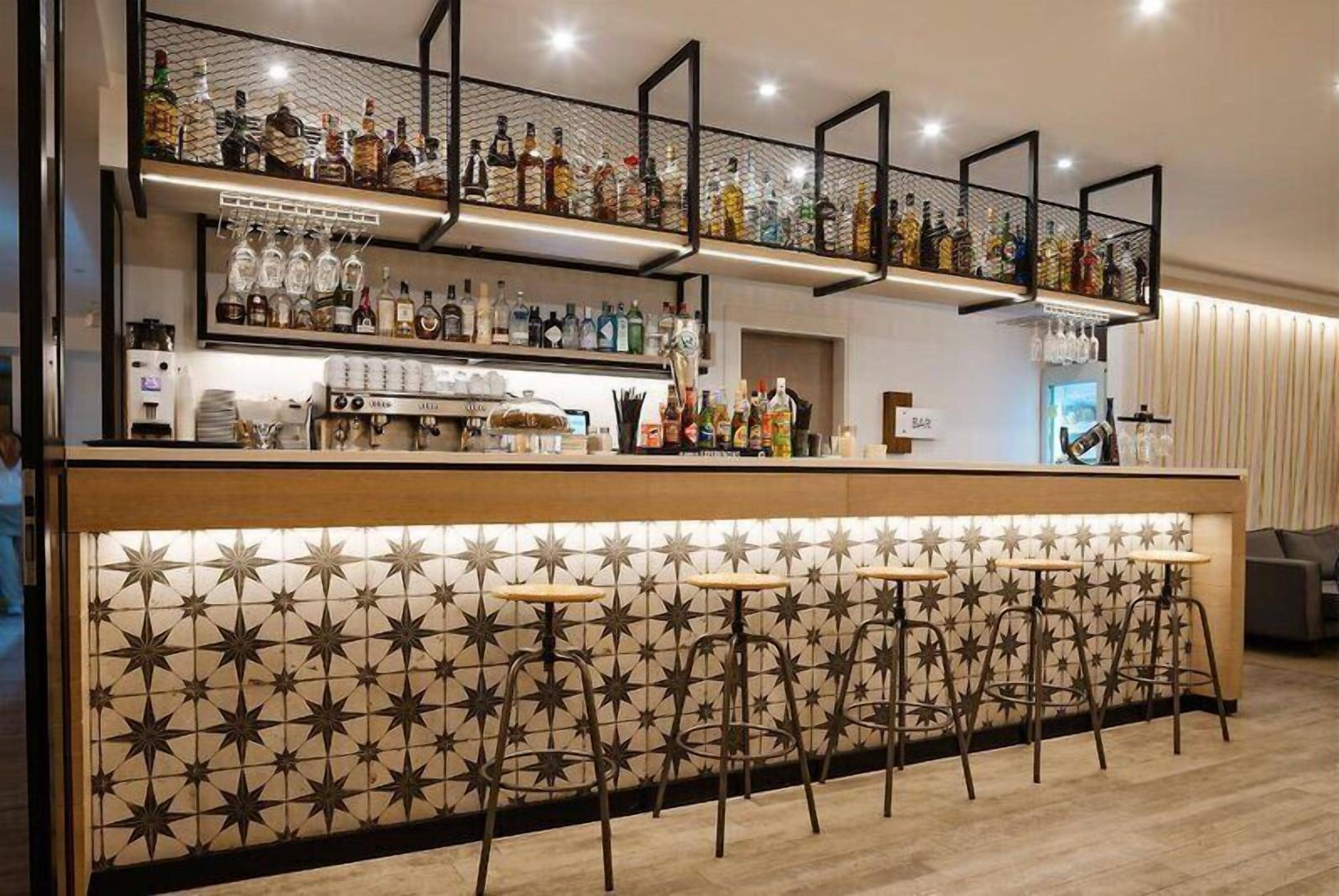 A bar area with a tiled backsplash, multiple liquor bottles, a coffee machine, and bar stools.