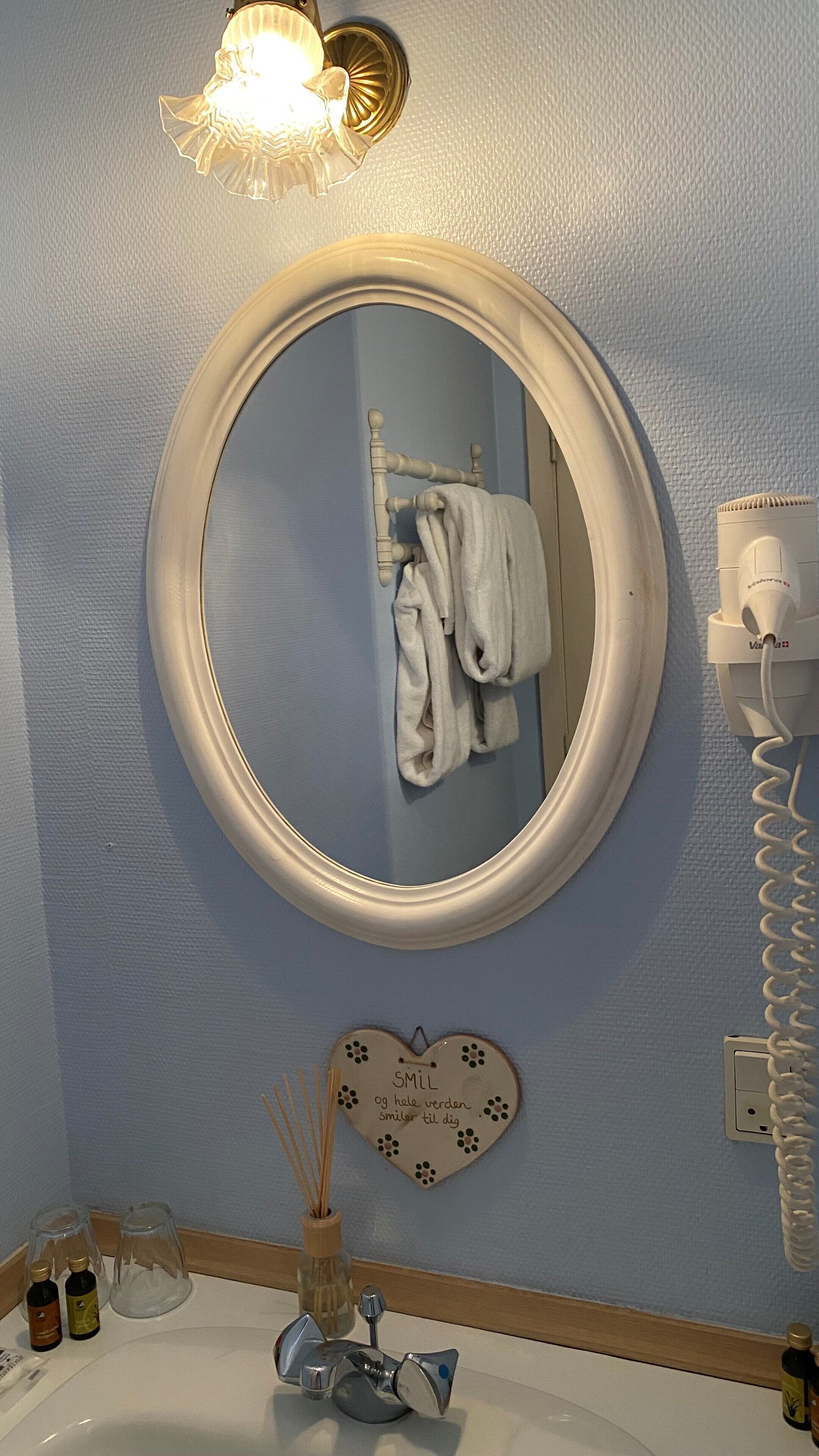 A bathroom with a round mirror, a towel rack, a vanity with a sink, and a hairdryer.