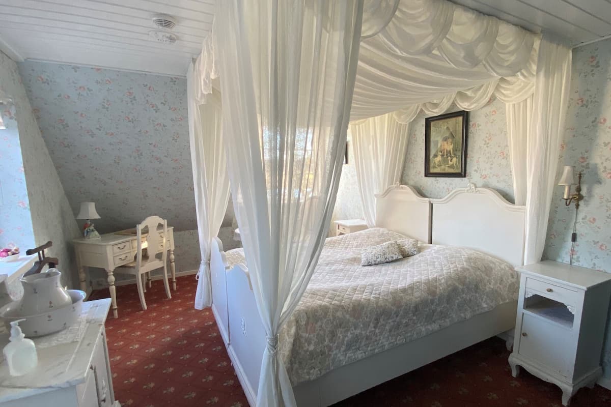 A bedroom with a four-poster bed, a nightstand, a dresser, a chair, and a bedside table.
