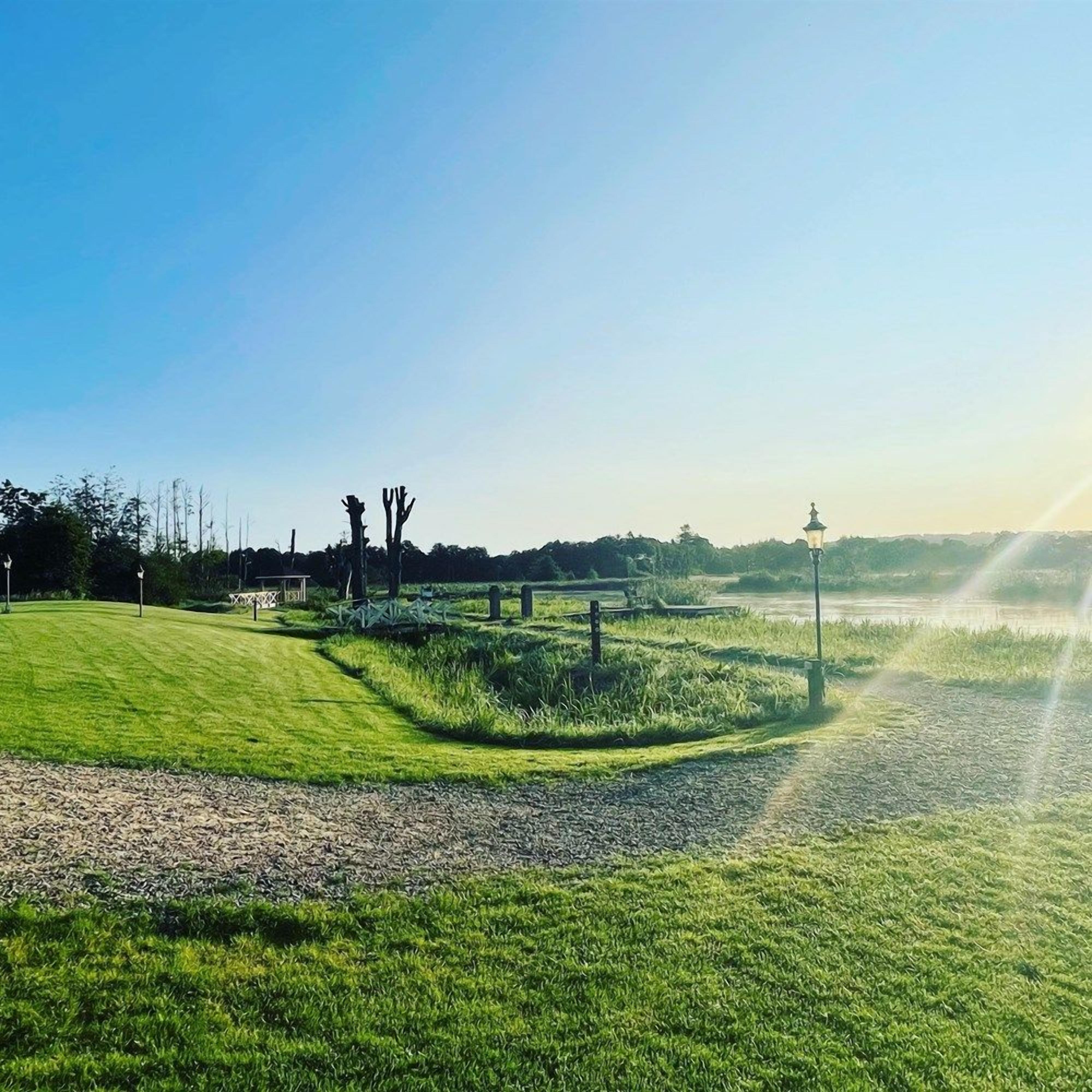 A well-maintained grassy area with a gravel path, a lamp post, and a fence in the distance.