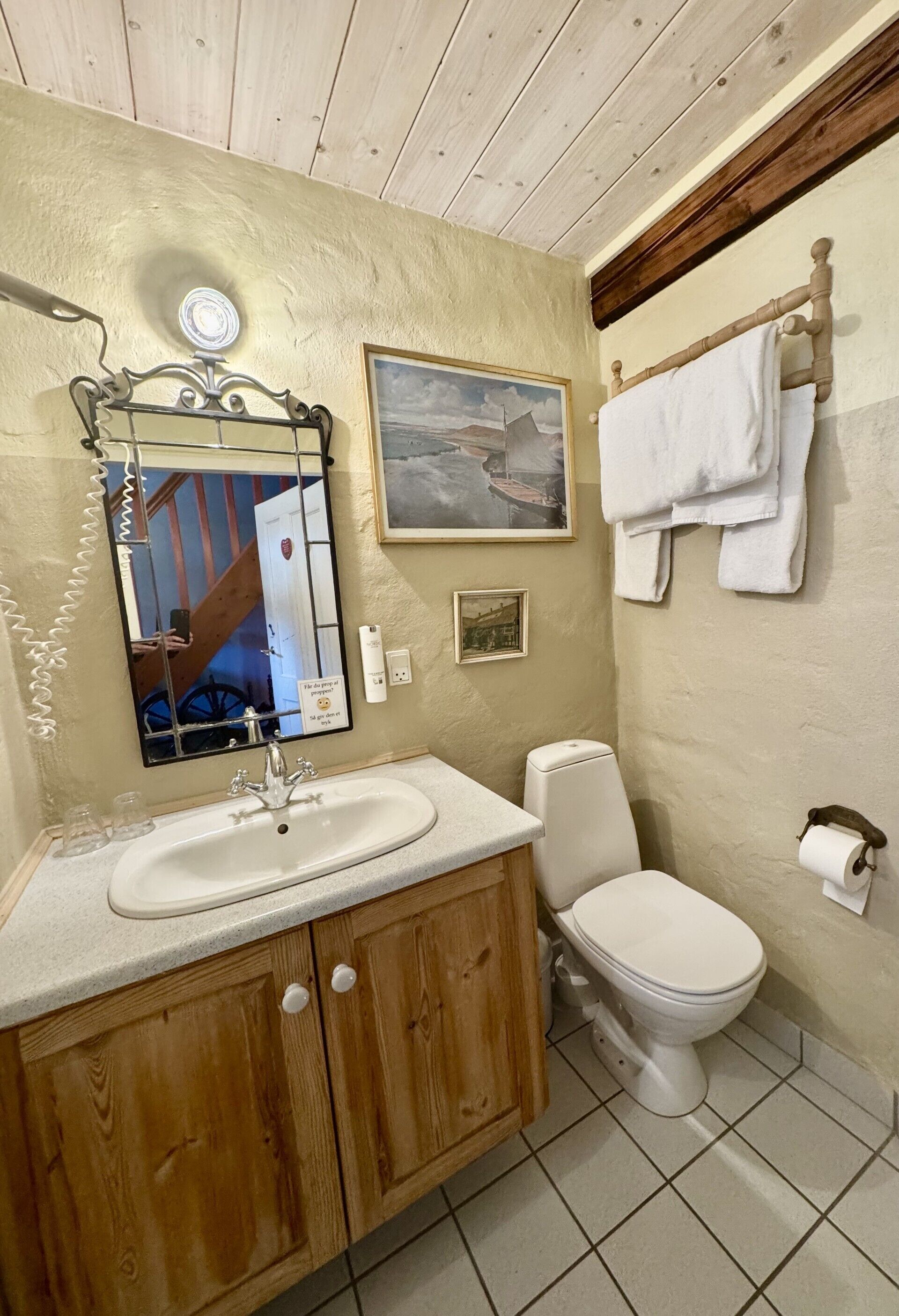 Ein Badezimmer mit einem Holzboden, einem weißen Waschbecken, einer Toilette und einem Spiegel mit Bilderrahmen.