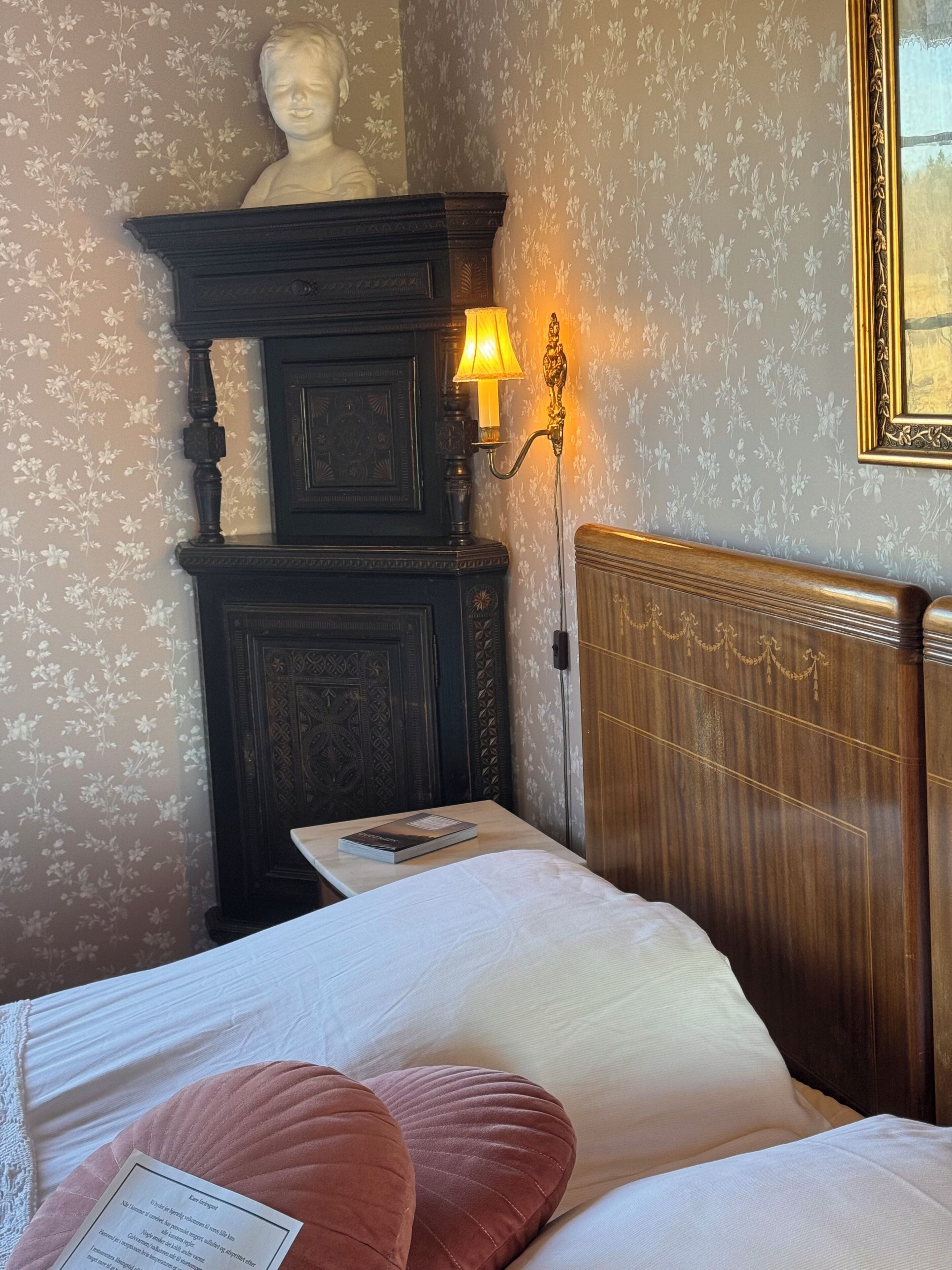 Ein Zimmer mit einem Bett, einem Nachttisch mit Lampe, einer Büste an der Wand und einem gerahmten Bild.