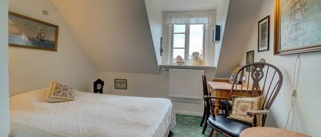 A bedroom with a bed, a chair, a table, and a window with a view.