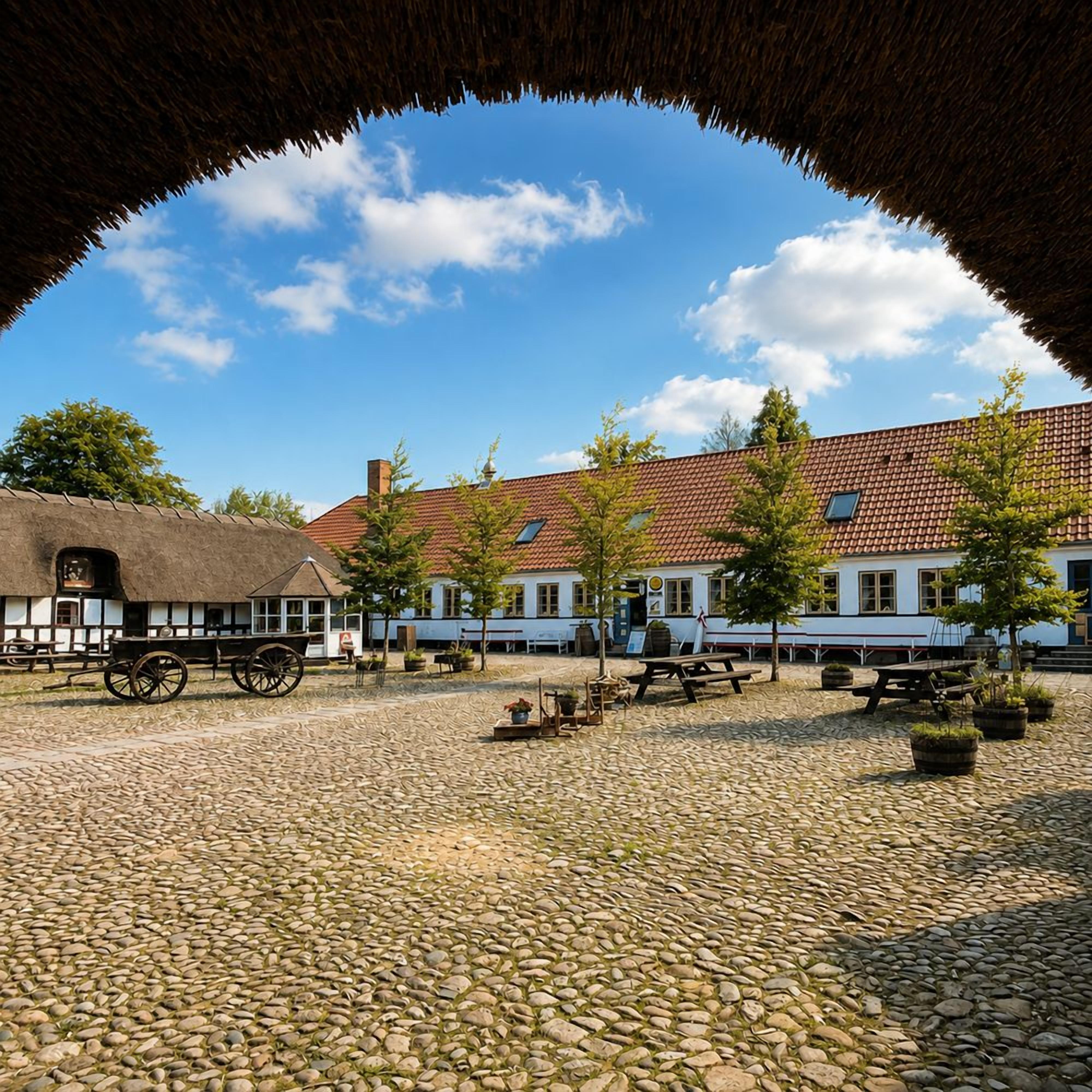 Ein Kopfsteinpflasterhof mit traditionellen Gebäuden, einem Gebäude mit Strohdach und einer Kutsche.