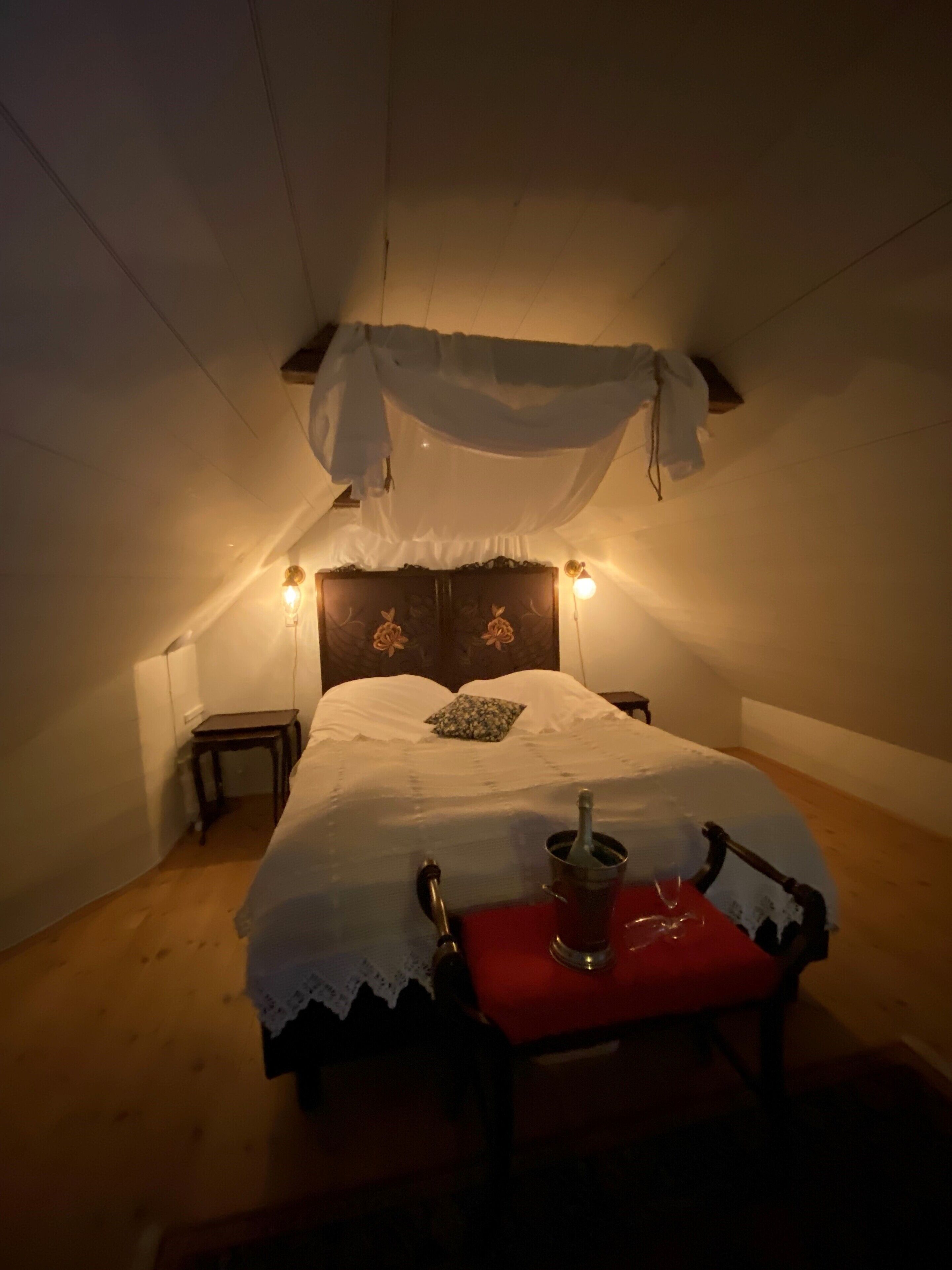 A bedroom with a bed, bedside lamps, a nightstand, and a chair with a red cushion.