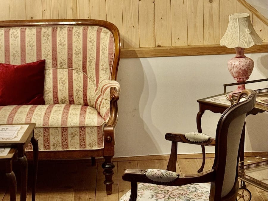 Une pièce avec un plafond en pente, des lambris en bois, un canapé, une chaise, une table et une lampe.